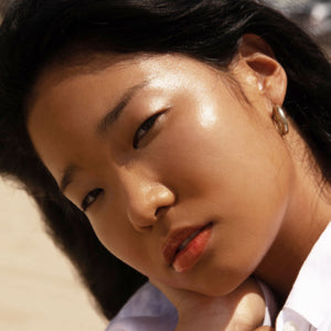 Closeup shot of girl with dewy cheeks wearing SuperDew Shimmer-Free Highlighter Balm by Tower28 Beauty